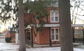 a brick house with a red roof is nestled between two tall trees in a snowy yard at Smithville Historical Museum and Inn