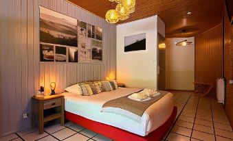 a large bed with a red headboard is in the middle of a room with tiled flooring and wooden walls at Logis le Chalet