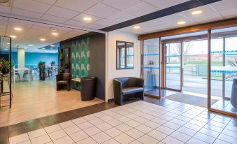 a modern , well - lit waiting room with black chairs and tables , large windows , and a check - in desk at Sure Hotel by Best Western St-Amand-Les-Eaux