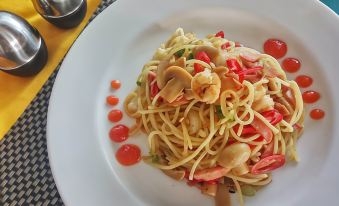 a white plate with a dish of spaghetti with red sauce and various toppings , including mushrooms and red peppers at Hotel Bandara Syariah
