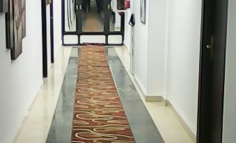 a hallway with a red and white carpet , a wooden door at the end , and paintings on the walls at Medina Hotel