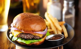 a black plate with a hamburger , fries , and a side of sauce on a wooden table at Airport Hotel Sydney