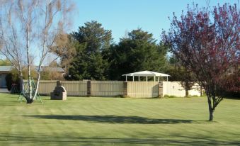 a large grassy field with trees and a gazebo , providing a picturesque setting for a backyard at Rest Point Motor Inn