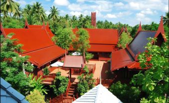 a beautiful red - roofed building surrounded by lush green trees and blue sky , creating a serene atmosphere at Baan Amphawa Resort & Spa