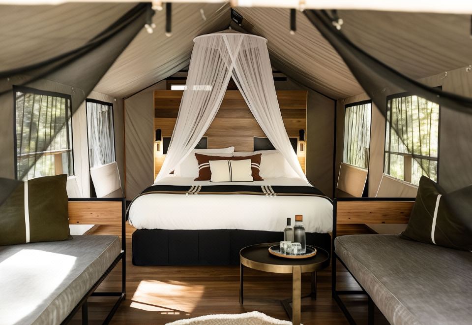 a large bed with a canopy is situated in a room with wooden walls and a table at Paperbark Camp