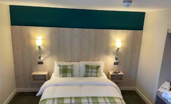 a bed with a green headboard and white sheets is shown in a room with two wall sconces at The White Horse