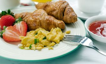 a plate of breakfast food , including eggs and croissants , is displayed on a table with a fork and glass of orange juice at Home2 Suites by Hilton Downingtown Exton Route 30