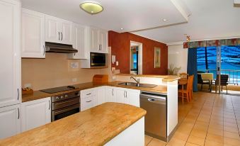 a well - equipped kitchen with white cabinets , wooden countertops , and a dining area in the background at Coolum Caprice