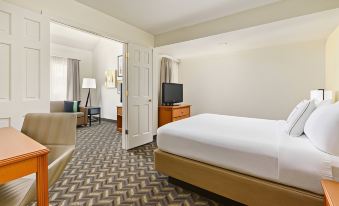 a large bed with white sheets is in a hotel room with a couch and a television at Residence Inn Hartford Windsor