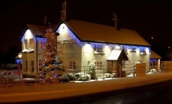 a snow - covered building with a christmas tree in front of it , illuminated at night at The Windmill Inn