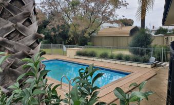a large swimming pool surrounded by a wooden deck , with trees and a house in the background at The Aston Motel Tamworth
