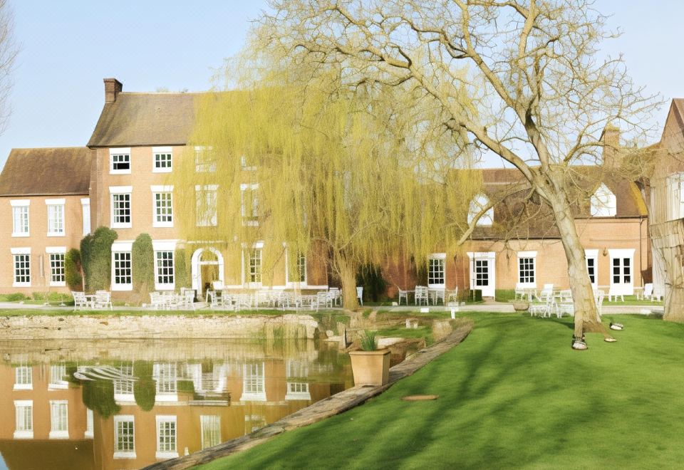 a large brick building with a tree in front of it , and a pond nearby at Corse Lawn House Hotel