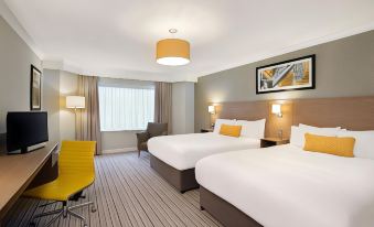 a modern hotel room with two beds , a chair , and a window , decorated with white bedding and yellow accents at Leonardo Hotel and Conference Venue Hinckley Island