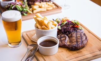 a dining table with a plate of food , including a steak and fries , accompanied by a glass of beer at Nightcap at Playford Tavern