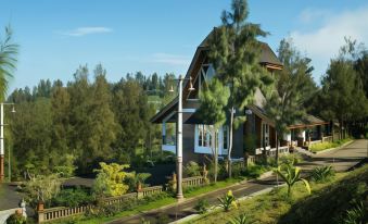 a large wooden house surrounded by trees and grass , situated on a hillside overlooking a body of water at Plataran Bromo