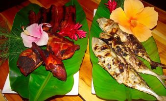 a wooden table with two plates of food , one containing grilled fish and the other containing a meat dish at Bantayan Island Nature Park and Resort
