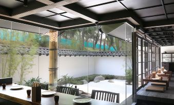 a dining room with a wooden table , chairs , and a potted plant in the corner at Delonix Hotel Karawang