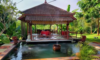 a small wooden gazebo surrounded by lush greenery , with a fountain in the middle of the pond at Tlogo Resort & Goa Rong View Ungaran