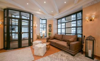 a spacious living room with brown leather couches , hardwood floors , and large windows that allow natural light to fill the space at Hotel Sailer