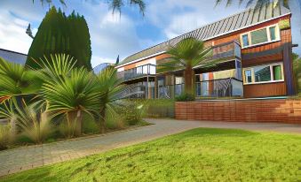 a modern building with a wooden exterior and large windows is surrounded by palm trees and green grass at Best Western Plus Oaklands Hotel