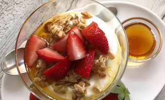 a glass bowl filled with strawberries , yogurt , and granola is placed on a white plate , accompanied by a small bowl of honey at Residence Inn Fort Lauderdale Weston