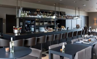 a modern bar with a long counter , several stools , and a variety of bottles and cups on the counter at Fletcher Hotel - Restaurant Nautisch Kwartier