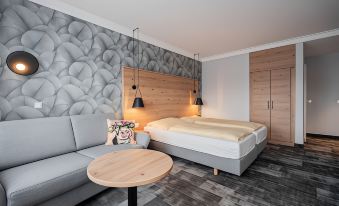 a modern bedroom with a gray couch , wooden table , and gray rug , along with wooden headboard and floor lamp at Hotel Adler - Paulas Alb
