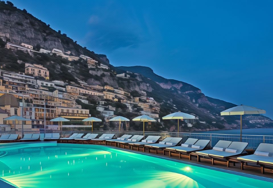 a large swimming pool with a row of lounge chairs and umbrellas next to it , overlooking a city at night at Covo dei Saraceni