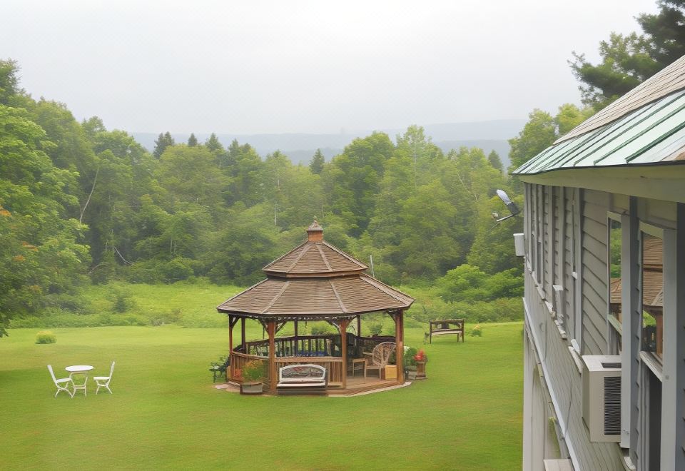 a wooden gazebo on a grassy field , surrounded by trees and a wooden gazebo in the background at Centennial House