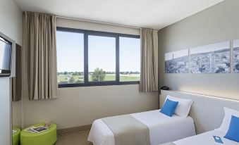 a hotel room with two twin beds , a window offering a view of the city , and a green bean bag chair at B&B Hotel Bologna