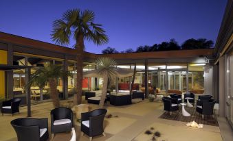 a modern outdoor area with black chairs and white cushions , surrounded by palm trees and large windows at Relais Bellaria Hotel & Congressi