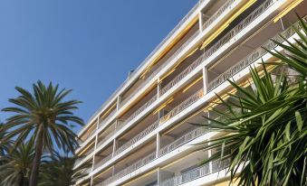 a large white and yellow building with many balconies , surrounded by palm trees and other greenery at Hotel Victoria