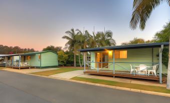 a green and blue house with a porch is surrounded by palm trees on a street at Nambucca River Village by Lincoln Place