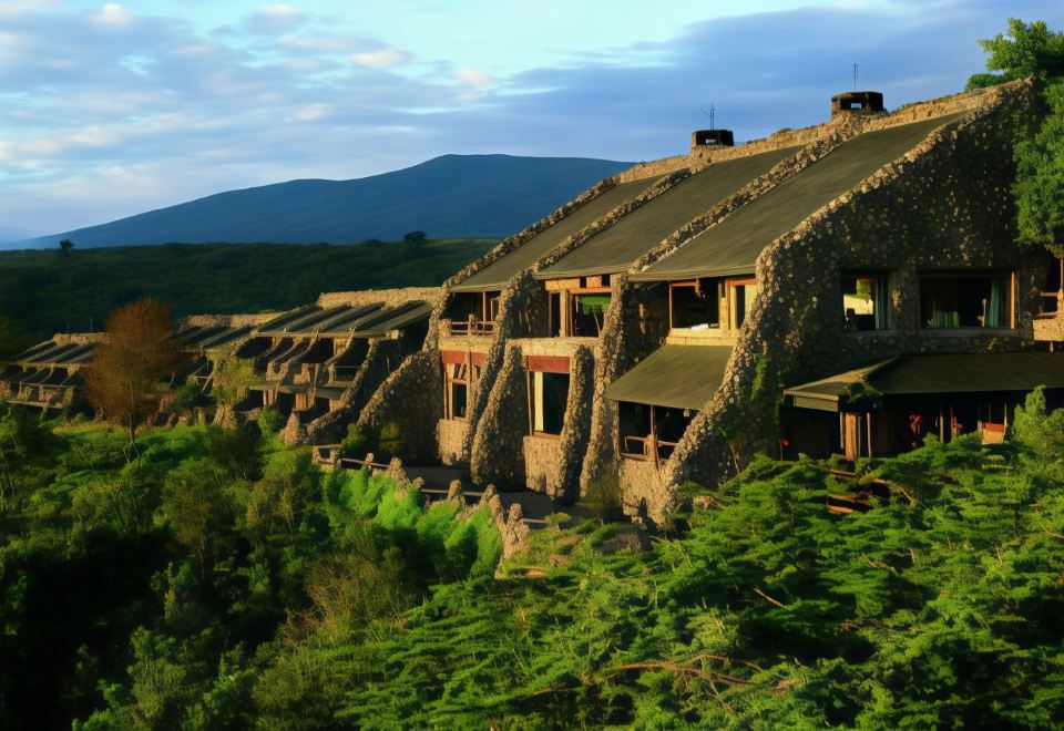 a large stone building with multiple balconies and balconies is perched on a hillside , overlooking a valley at Ngorongoro Serena Safari Lodge