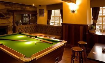 a pool table is in the middle of a room with wooden chairs and stools at The Engine Inn