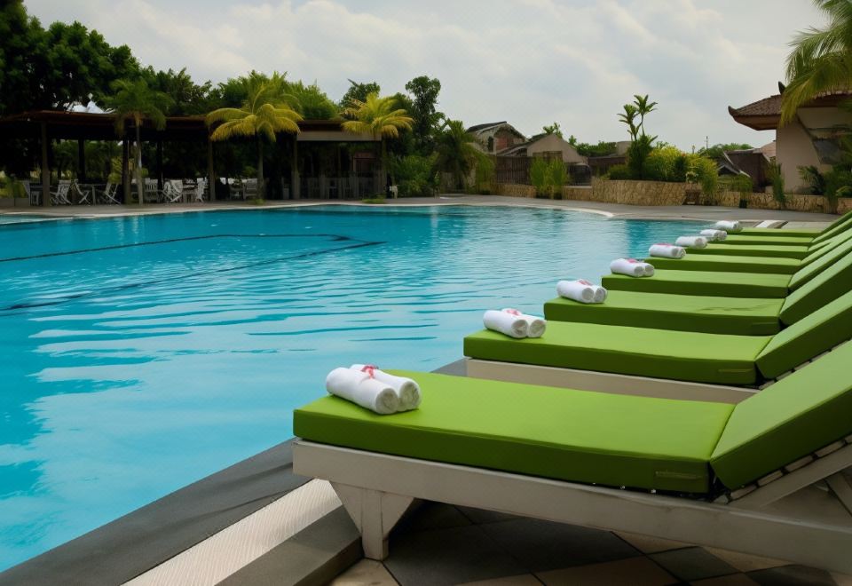 a row of lounge chairs with green cushions are lined up next to a pool at The Sunan Hotel Solo
