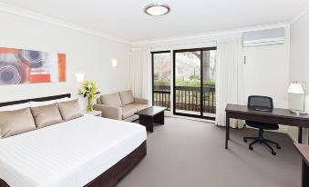 a modern hotel room with a large bed , couch , and sliding glass doors leading to a balcony at Ibis Styles Canberra Tall Trees