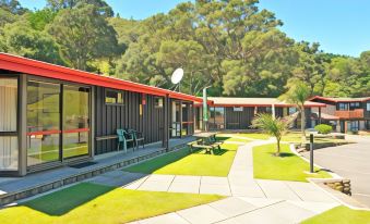 a modern , black and red building with large windows surrounded by green grass and trees , as well as outdoor furniture on the ground at Anglers Lodge