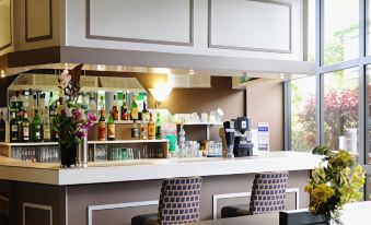 a bar with a variety of bottles and glasses on the counter , as well as chairs for patrons to sit in at Comfort Hotel Aeroport Lyon St Exupery