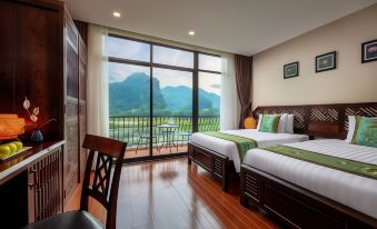 a room with two beds , one on each side of the room , and a large window overlooking a beautiful view at Tam Coc La Montagne Resort & Spa