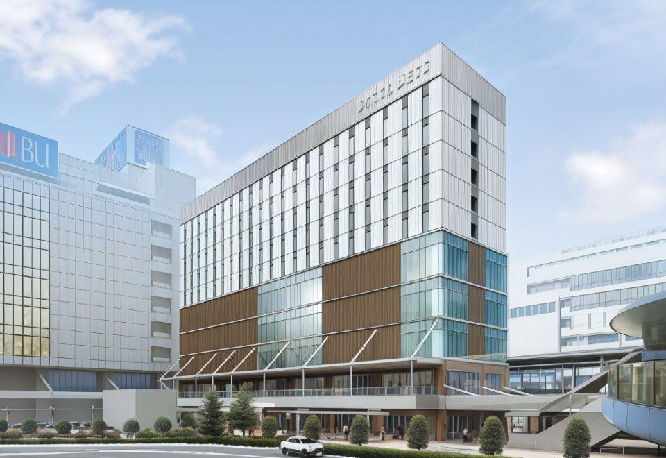 a large , modern building with multiple floors and glass windows is surrounded by trees and a street at JR-EAST HOTEL METS FUNABASHI