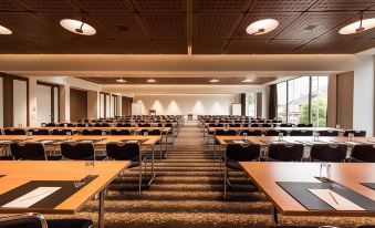 a large conference room with rows of tables and chairs , a projector screen , and hanging lights at Hotel Ambassador