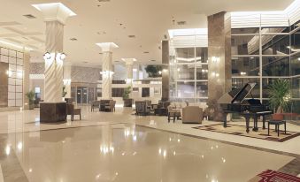a large , modern hotel lobby with high ceilings , white columns , and a piano in the center of the room at Forbis Hotel