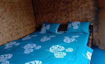 a bed with blue and white sheets , pillows , and a wicker headboard , surrounded by bamboo walls at De Salak Homestay