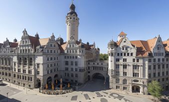 a large building with a tower and multiple buildings surrounding it , including a restaurant and an event space at NH Leipzig Zentrum