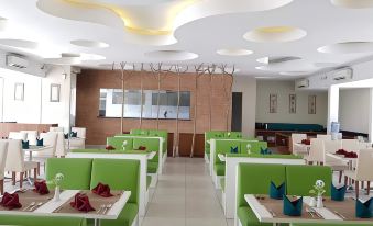 a modern restaurant with green booths and white tables , featuring a large screen in the background at Front One Resort Magelang