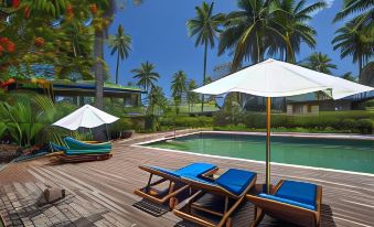 a wooden deck with lounge chairs and umbrellas , leading to a pool surrounded by palm trees at Maravu Taveuni Lodge