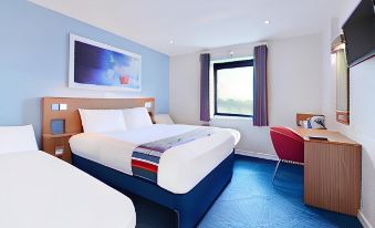 a hotel room with a blue and white color scheme , featuring two beds , a desk , and a window at Travelodge Oswestry