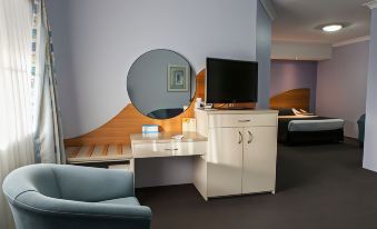 a modern hotel room with a white desk , chair , and tv , along with a round mirror on the wall at Shellharbour Village Motel