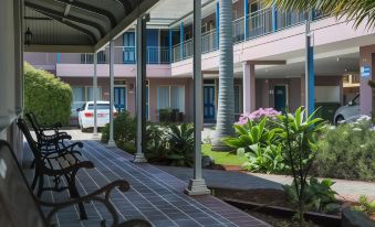 a courtyard with a brick walkway leading to a building , surrounded by potted plants and trees at Shellharbour Village Motel